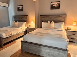 Ein Doppelzimmer mit zwei Betten, jeweils mit Holz Kopfteil, weißer Bettwäsche und Nachttischlampen.