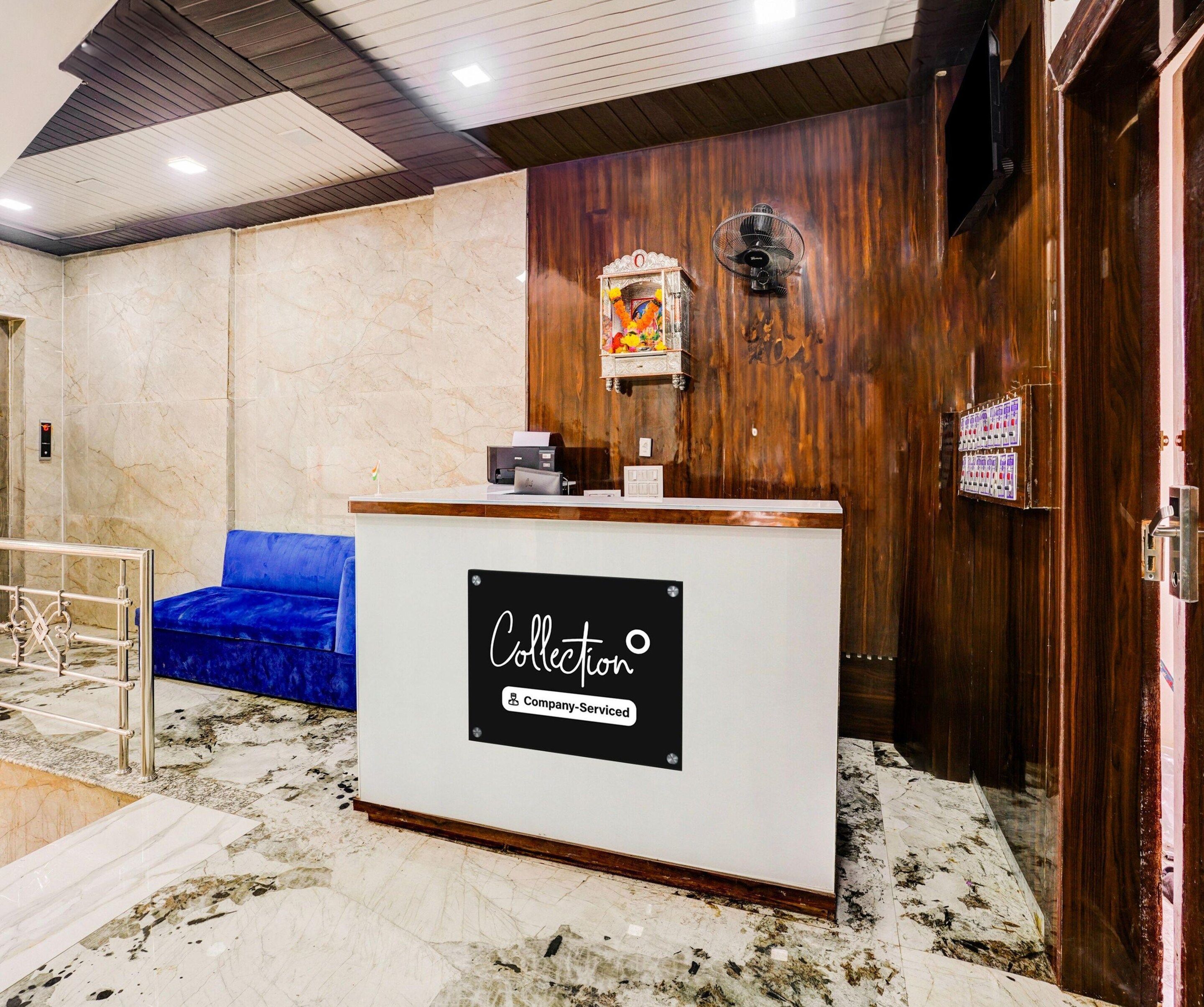A reception desk with a sign indicating it's company-serviced, a blue sofa, a wooden wall, and a fan.