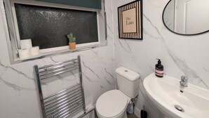 Une salle de bain comprenant des toilettes, un lavabo, un miroir, une fenêtre et un tableau encadré au mur.