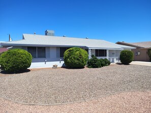 A single-story house with a grey roof, a covered porch, and a gravel driveway. - Sunshine Sanctuary - Peace, Quiet & Sunshine - 55+ Active Senior Community (Sun City)