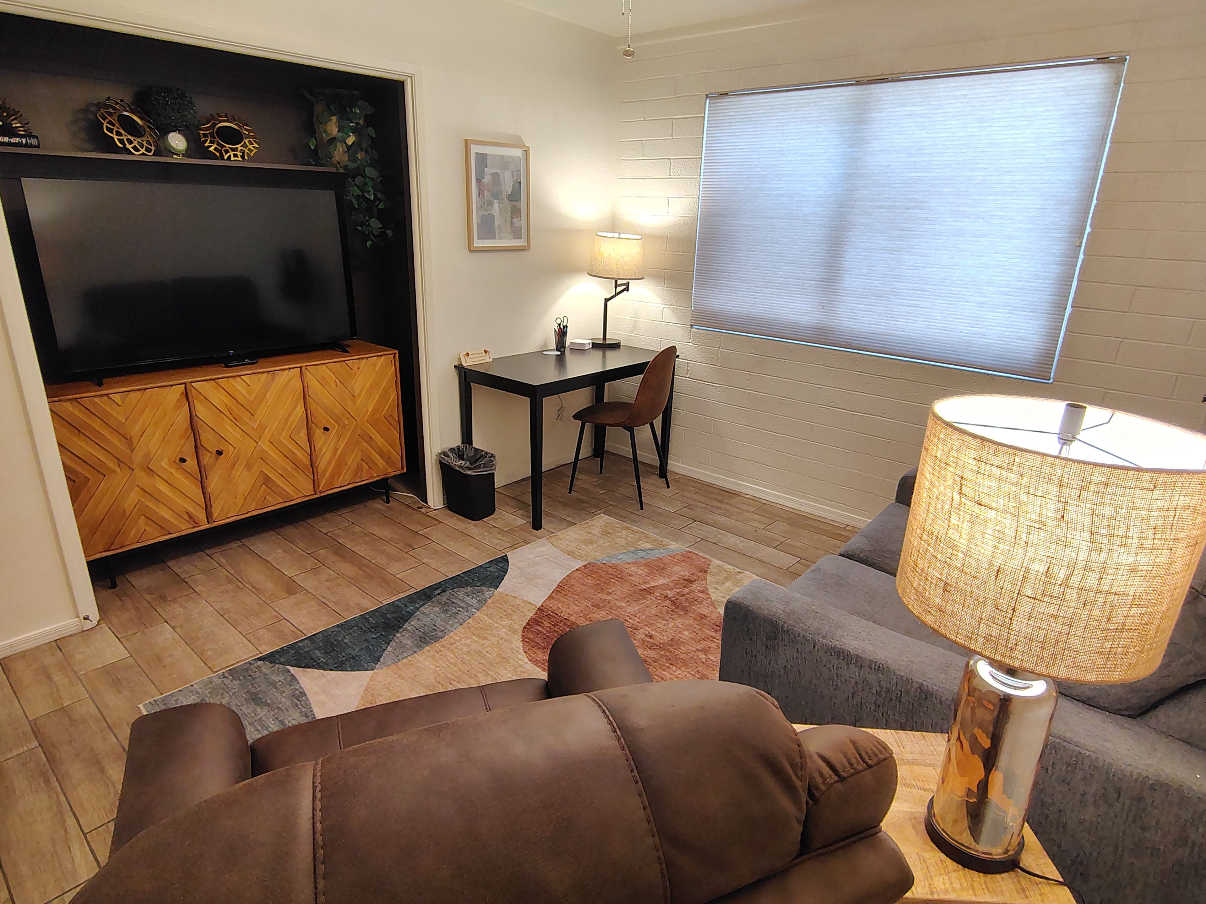A living room with a sofa, a television, a table with a lamp, and a window with blinds.
