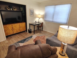A living room with a sofa, a television, a table with a lamp, and a window with blinds.