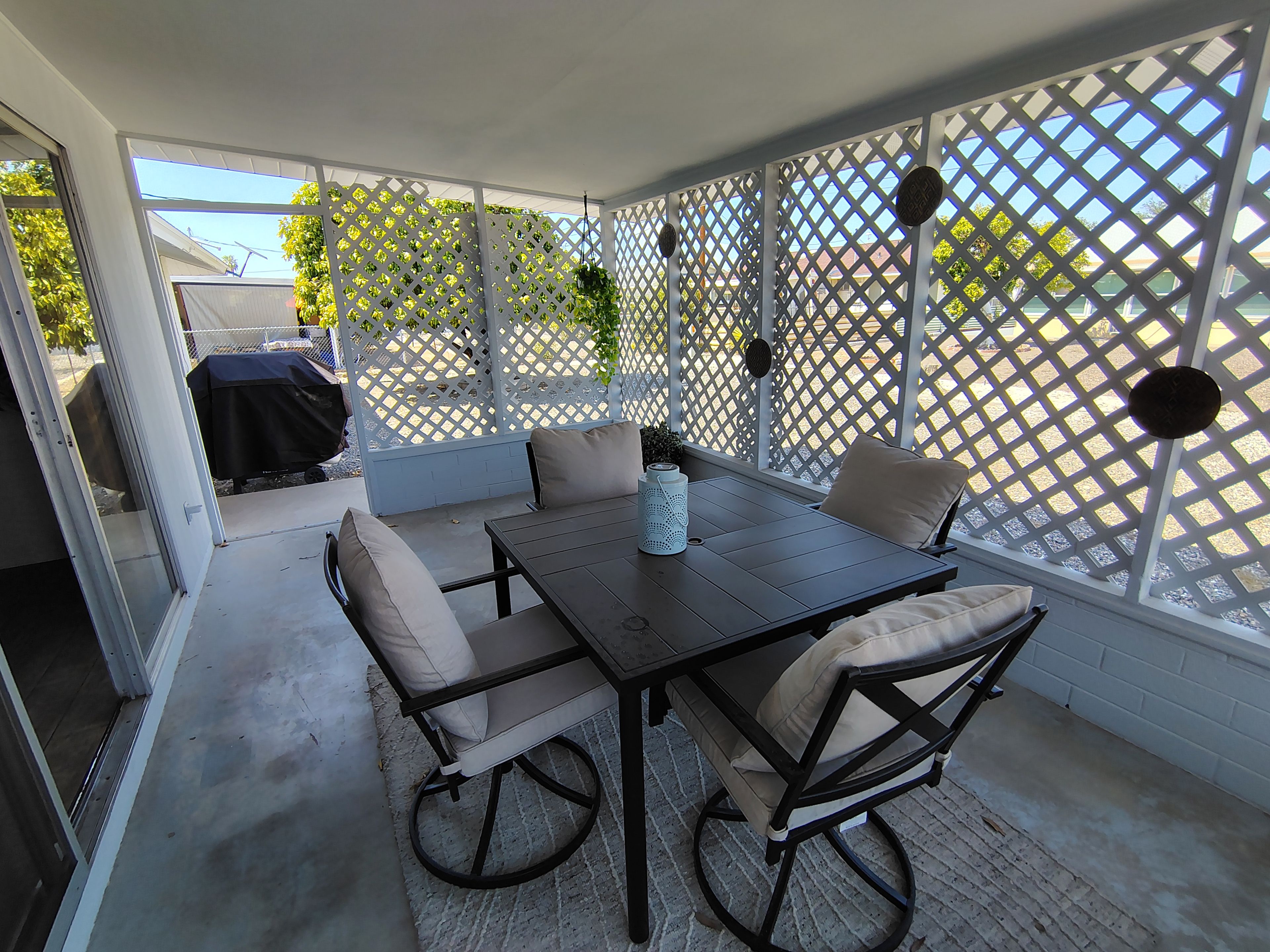 An outdoor patio with a table and chairs, a covered grill, and a lattice screen.