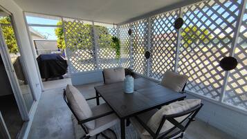 An outdoor patio with a table and chairs, a covered grill, and a lattice screen.