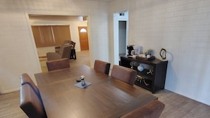 Uma área de refeições com mesa de madeira e cadeiras de couro, um cantinho para café e um pequeno armário com objetos decorativos.