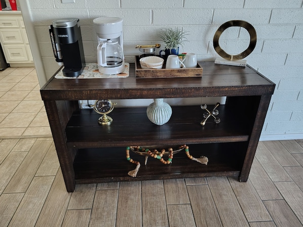 A dark wooden coffee table with a coffee maker, a clock, decorative items, and a potted plant.