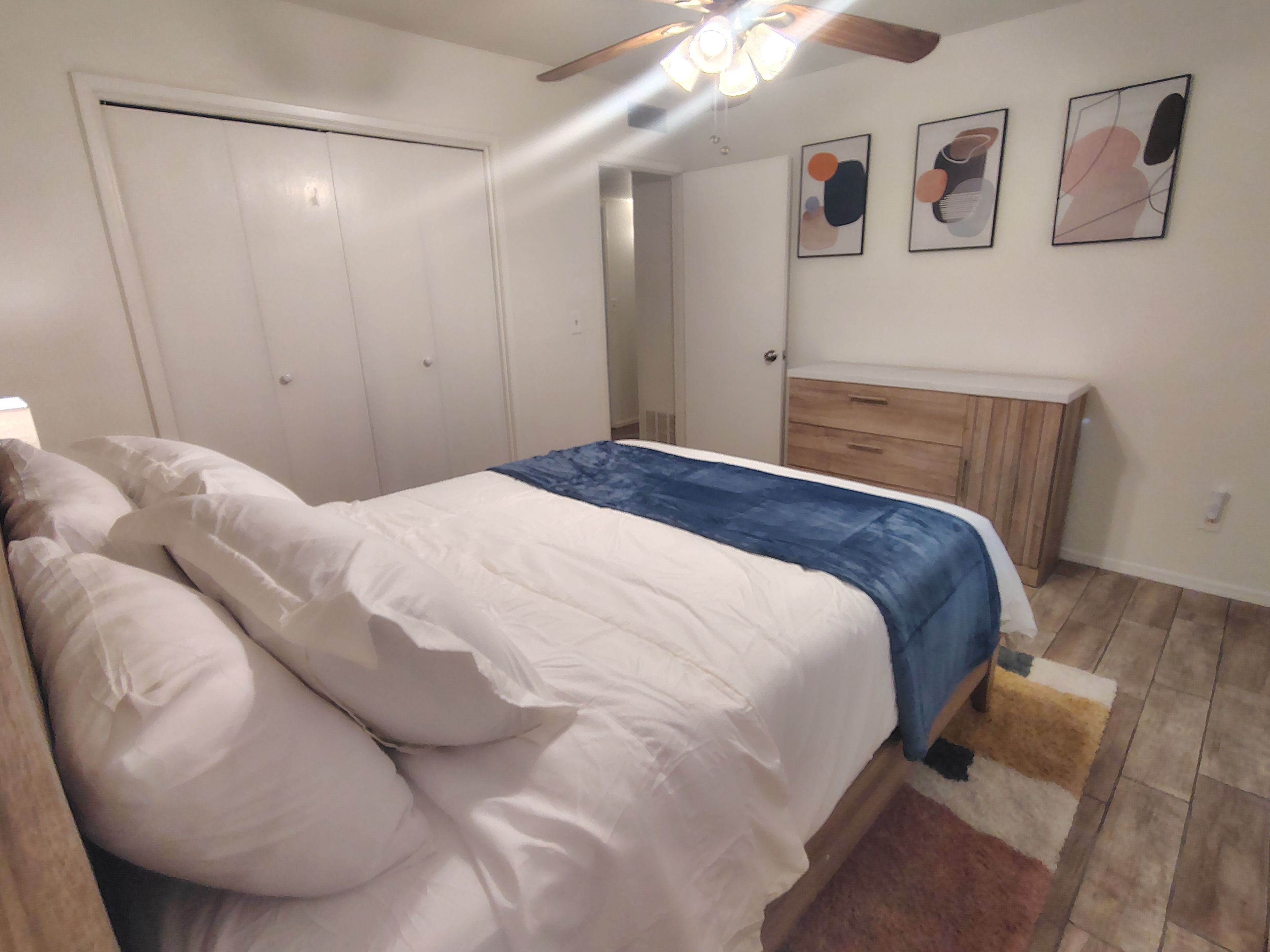 A bedroom with a bed, a wooden dresser, a ceiling fan, and a door.