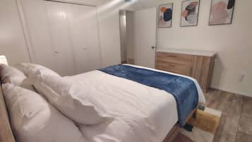 A bedroom with a bed, a wooden dresser, a ceiling fan, and a door.