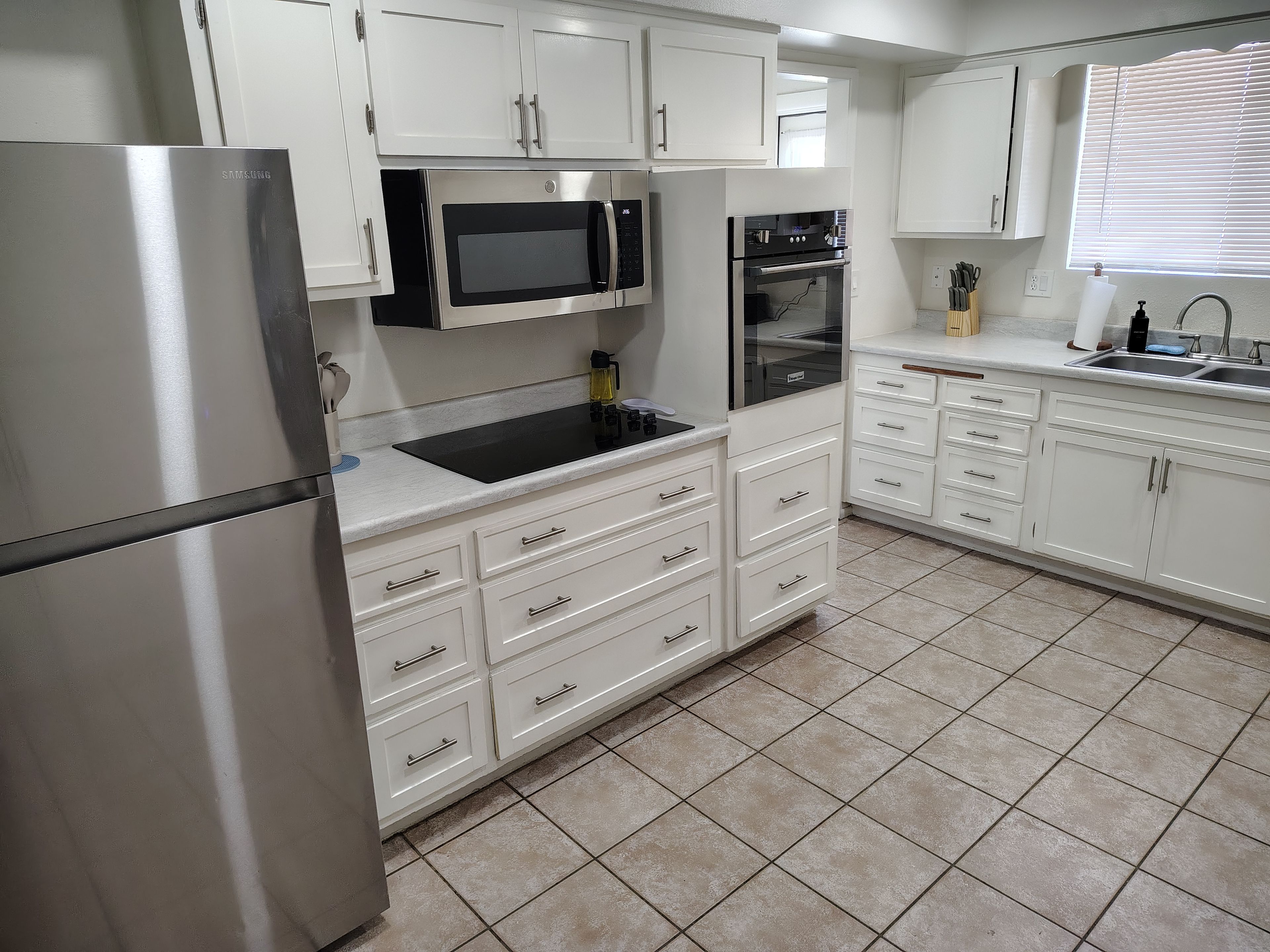 A modern kitchen with white cabinetry, stainless steel appliances, and a tiled floor.
