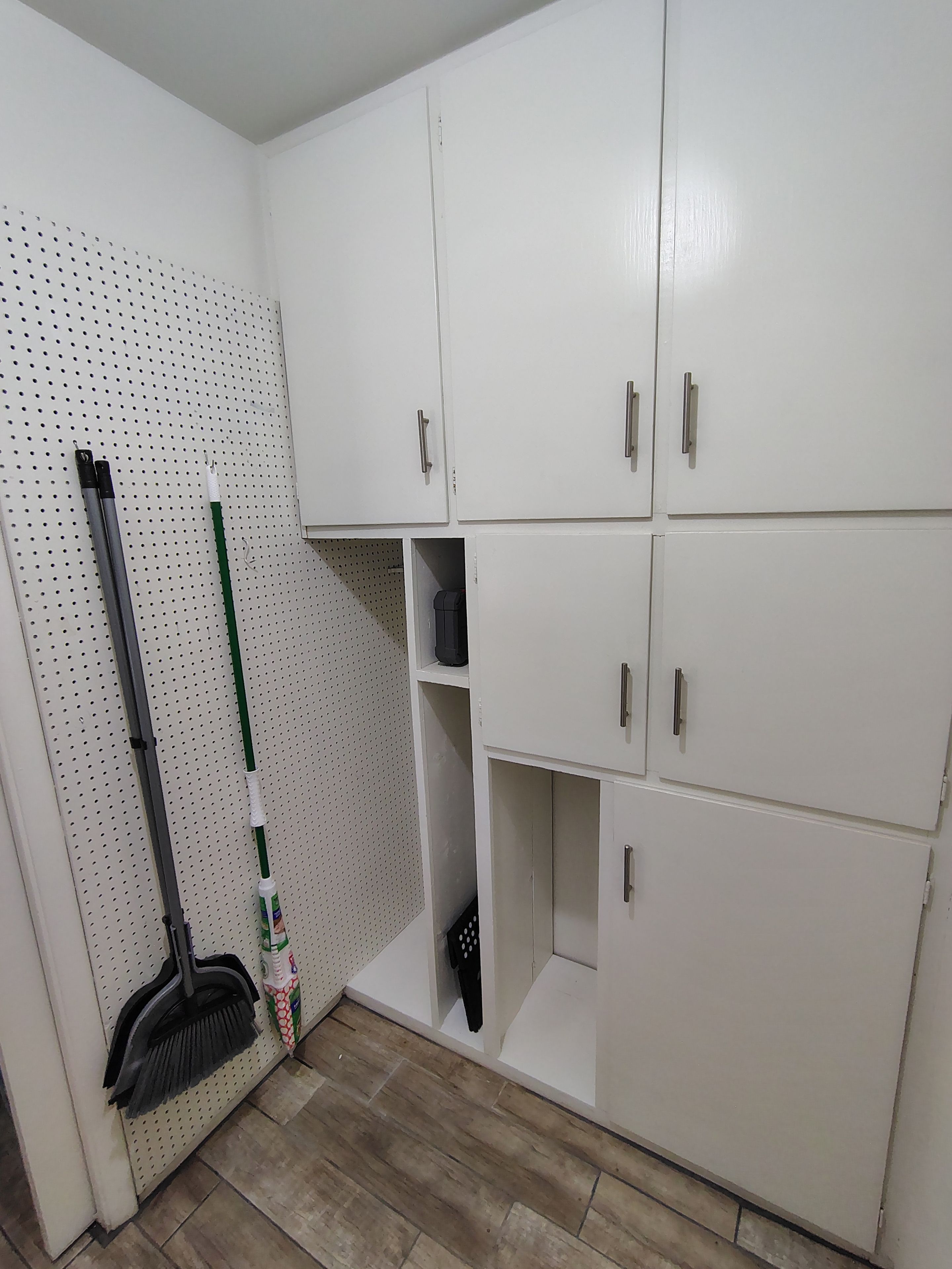 A room with white cabinets, a broom, and a mop on the wall.