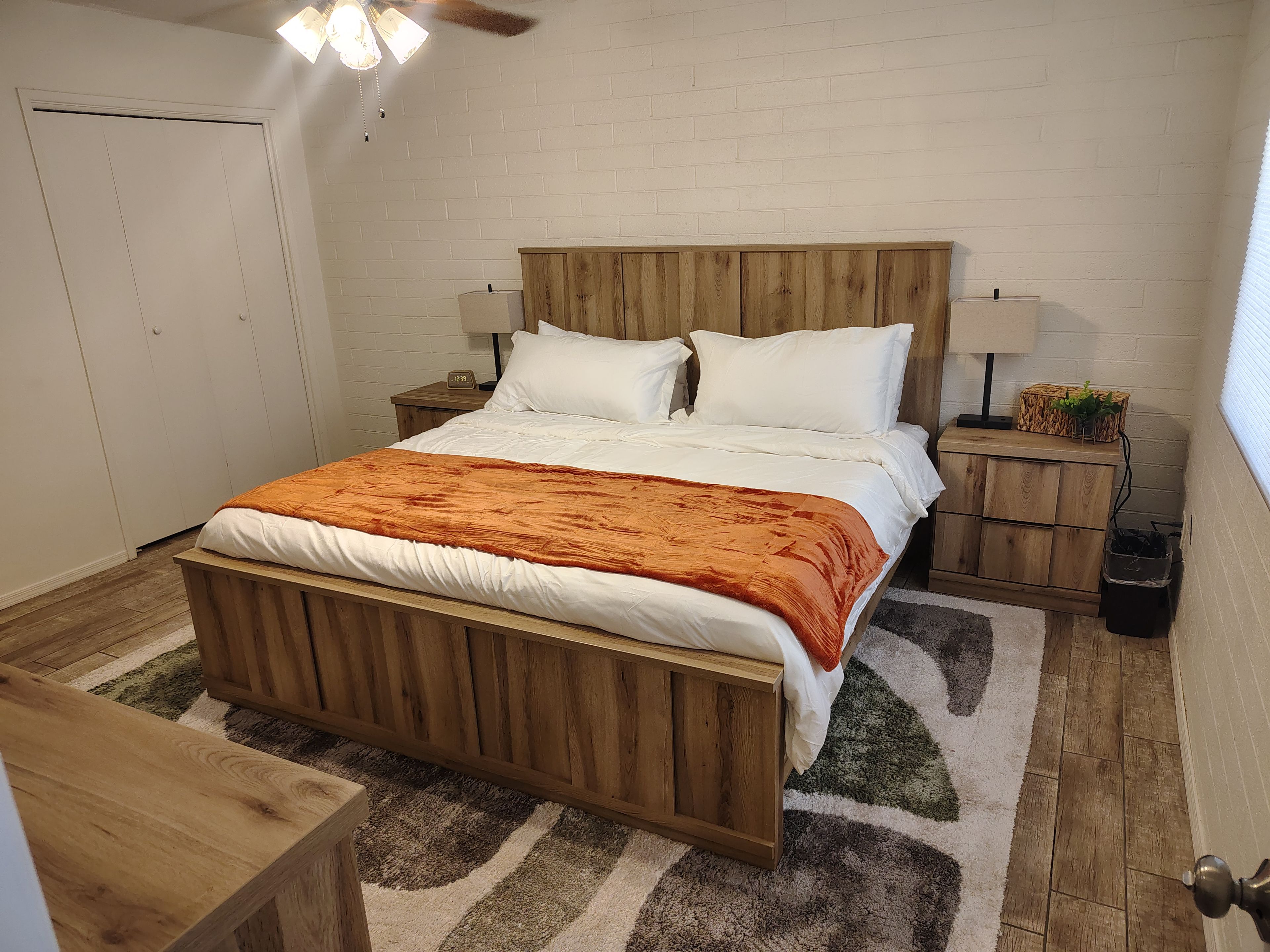 A bedroom with a wooden bed, white bedding, a nightstand with a lamp, and a small wooden cabinet.
