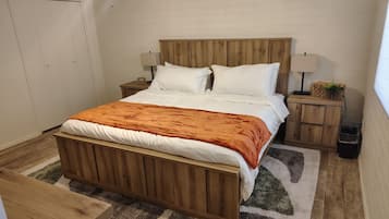 A bedroom with a wooden bed, white bedding, a nightstand with a lamp, and a small wooden cabinet.