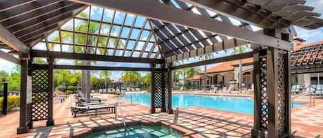 A covered pool area with a hot tub, lounge chairs, and a pergola structure.