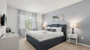 Ein modernes Schlafzimmer mit einem großen Bett, zwei Nachttischen, einem Flachbildfernseher und einem Fenster mit Vorhängen.