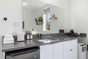 A modern bathroom with a large mirror, a sink, a towel rack, and a coffee machine.