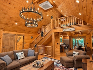 A wooden cabin interior with a staircase, a chandelier, a welcome sign, and a dining area. - Adirondack BearDen - 6BR 4BA Ski/Hike Family Cabin (Jay)