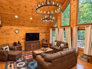 Ein gemütliches Cabin-Interieur mit einem großen Fernseher, Ledersofas, einer Holzzieldecke und einem Kronleuchter.