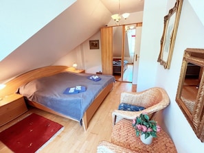 Un dormitorio con una cama, una silla, un tapete rojo, un espejo y una puerta que da a otra habitación.