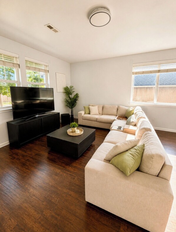 A living room with a large flat-screen TV, a dark coffee table, a beige sofa, and a potted plant. - Peaceful 3-bedroom house in charming Yelm perfect for relaxing getaway (Yelm)