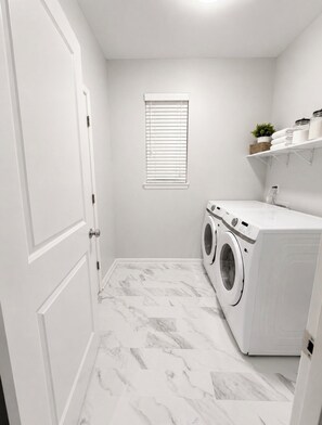 A laundry room with a washing machine, dryer, and a window with blinds. - Peaceful 3-bedroom house in charming Yelm perfect for relaxing getaway (Yelm)