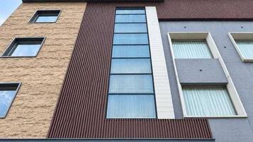 Un immeuble à plusieurs étages dont la façade est un mélange de briques et de panneaux, doté de grandes fenêtres et surmonté d’un toit plat.