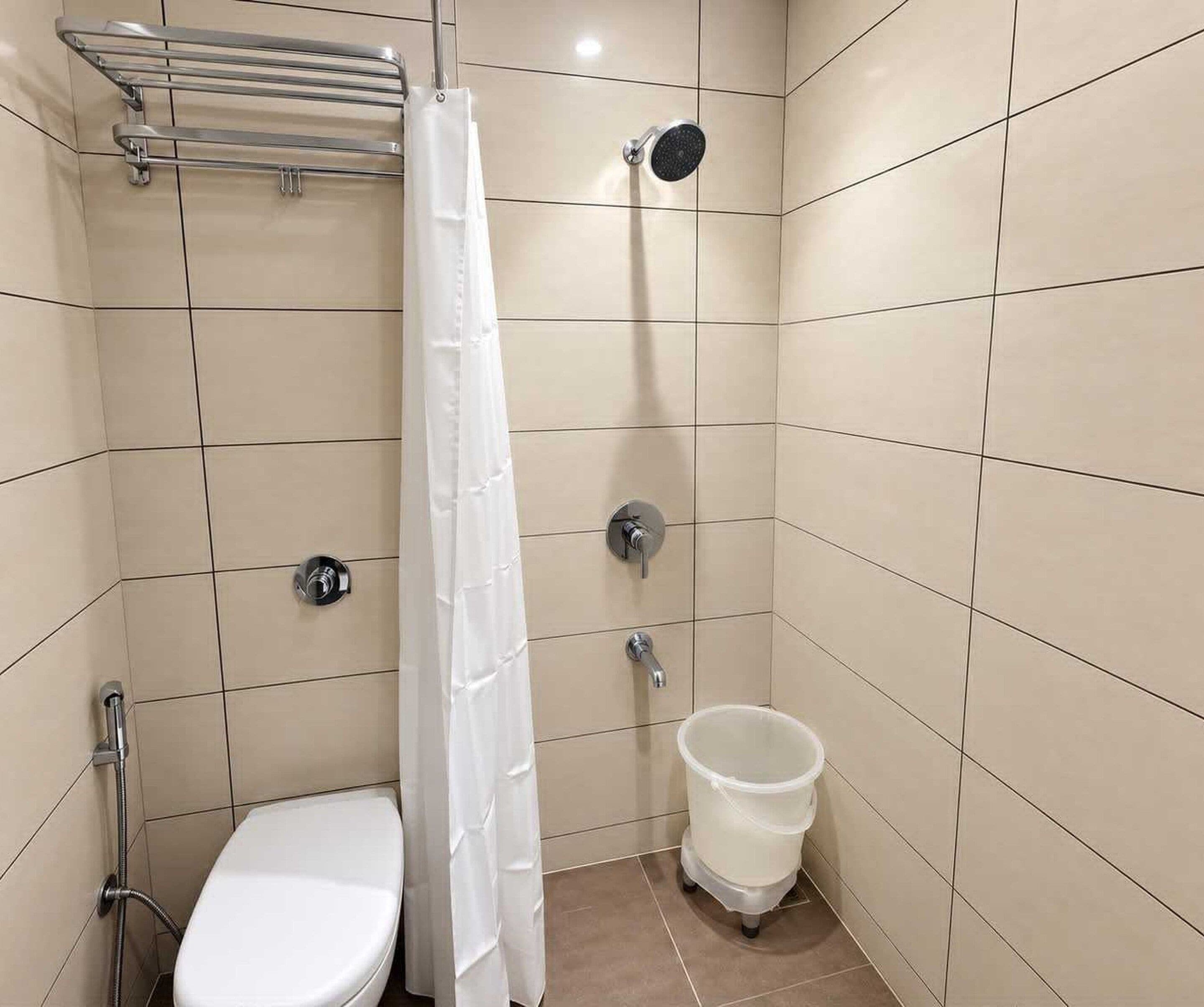 A small, tiled bathroom with a toilet, a shower, and a toilet paper holder.
