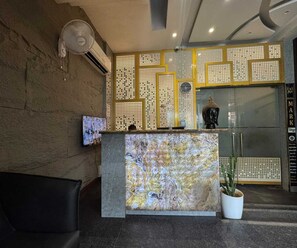 Ein Empfangsbereich mit Marmor-Theke, einer Topfpflanze und einer Wand mit geometrischem Muster.