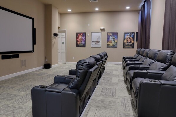 Ein Heimkinozimmer mit einer großen Leinwand, Liegesesseln aus Leder und Filmplakaten an der Wand.