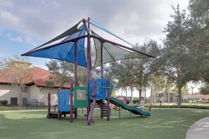 Ein Spielplatz mit Rutsche, Klettergerüsten und einem schattigen Bereich.
