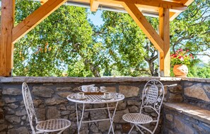 A stone wall with a metal table and chairs, a potted plant, and a wooden pergola structure. - Cozy home in Stankovci with private swimming pool, can be inside or outside (Stankovci)