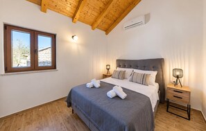A bedroom with a large bed, wooden flooring, a stone wall, and a window with a view. - Cozy home in Stankovci with private swimming pool, can be inside or outside (Stankovci)
