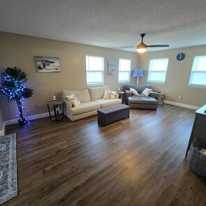 A living room with a beige sofa, a gray armchair, a small table, and a ceiling fan. - Kentucky Lake Vista (Gilbertsville)