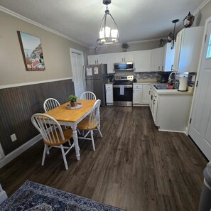A kitchen with white cabinets, a wooden dining table, and a hanging light fixture. - Kentucky Lake Vista (Gilbertsville)