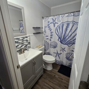 A bathroom with a white sink, a toilet, and a shower curtain with a sea-themed design. - Kentucky Lake Vista (Gilbertsville)