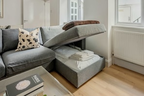 A modern living room with a grey sofa, a small table with a book, and a radiator. - 2-bed Flat Near Regent's Park - Patio - Sleeps 6 (London)