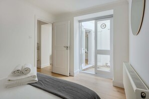 A hotel room with a bed, a radiator, a door leading to a balcony, and a towel on the bed. - 2-bed Flat Near Regent's Park - Patio - Sleeps 6 (London)