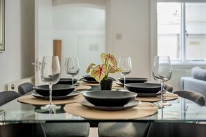 Una mesa de comedor con platos negros, copas de vino transparentes y una planta en maceta con hojas amarillas y rojas.