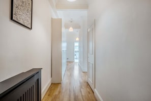 Un couloir avec un plancher en bois, des murs blancs et une rambarde noire sur le côté gauche.