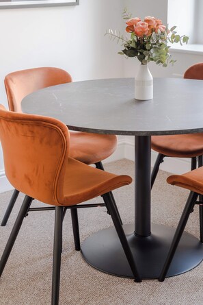 A round table with a white vase of flowers, surrounded by four orange chairs with black legs. - The Foley Residence - Fitzrovia - by Frankie (London)
