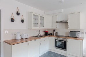 A modern kitchen with white cabinets, a wooden countertop, a built-in oven, a microwave, and a coffee maker. - The Foley Residence - Fitzrovia - by Frankie (London)