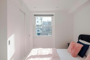 Un dormitorio con cama, ventana y vista a edificios.