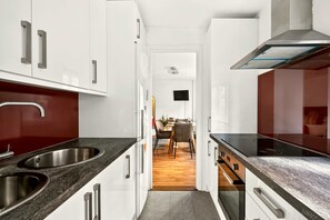 A modern kitchen with stainless steel appliances, a dining area with a wooden table and chairs, and a view into the living room. - Covent Garden Studio · Sleeps 3 · Floral St (London)