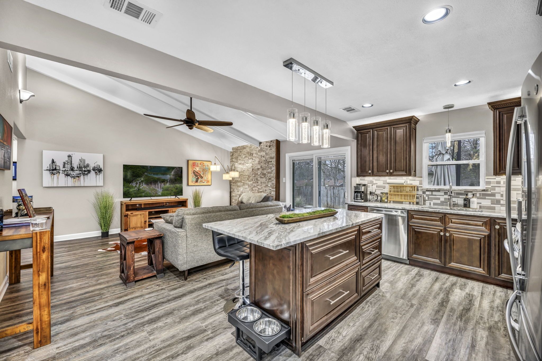 A modern kitchen with a large island, dark wood cabinets, and a stone backsplash.