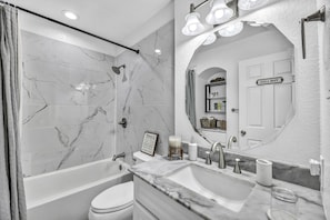 Un baño moderno con bañera, inodoro y tocador con un espejo grande.