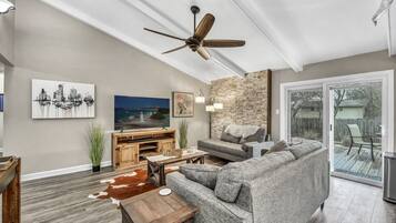A spacious living room with a ceiling fan, a stone accent wall, a large window, and a sliding glass door leading to a deck.