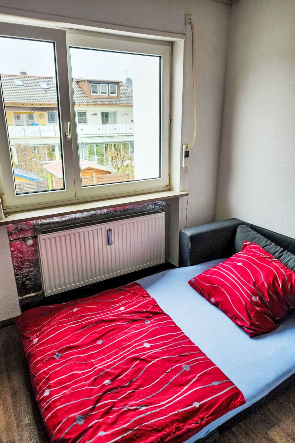 Ein kleines Zimmer mit einem Bett, einem Fenster und einer Heizung.