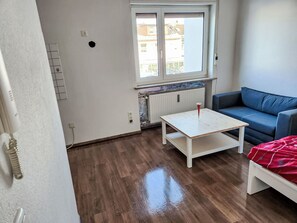 A room with a blue sofa, a white table, and a window with a view of buildings. - Einfache 1-Zimmer Wohnung by Interhome (Bad Wörishofen)