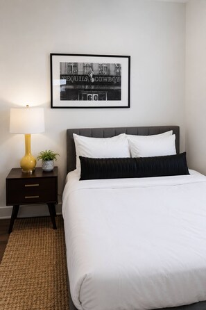 A neatly arranged bedroom with a bed, a nightstand with a lamp, and a framed picture on the wall. - Sleeps 10 Near Broadway | Hart Suites Unit #2 (Nashville)