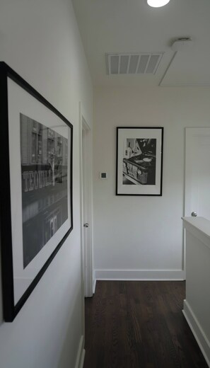 A hallway with two framed pictures on the wall, a door, and a ceiling vent. - Sleeps 10 Near Broadway | Hart Suites Unit #2 (Nashville)