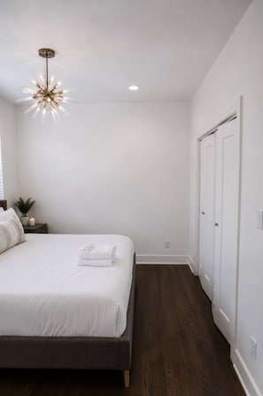 A bedroom with a bed, a nightstand with a plant, a wall-mounted light fixture, and a door. - Sleeps 10, free parking — Hart Suites #4 (Nashville)